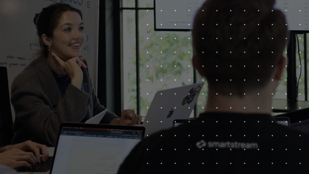 Two Colleagues Sit at a Table in a Meeting Room with Laptops Open the Woman Smiling As She Talks